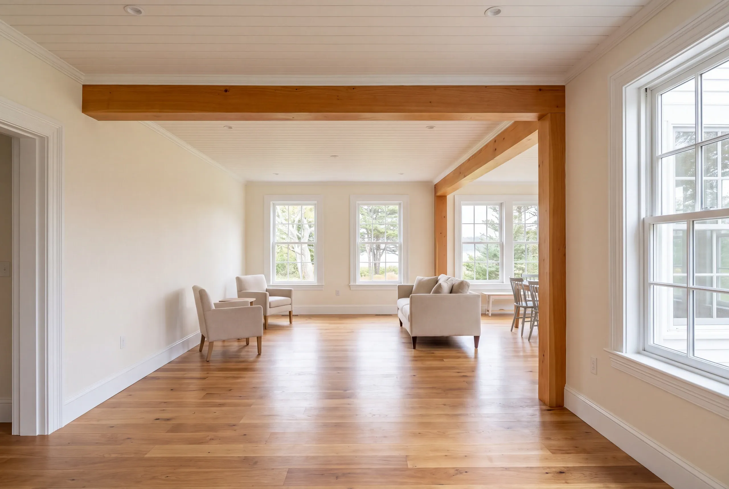 Remodeling company Rockport Maine: living room with a natural post and beam, cream armchairs and a linen sofa