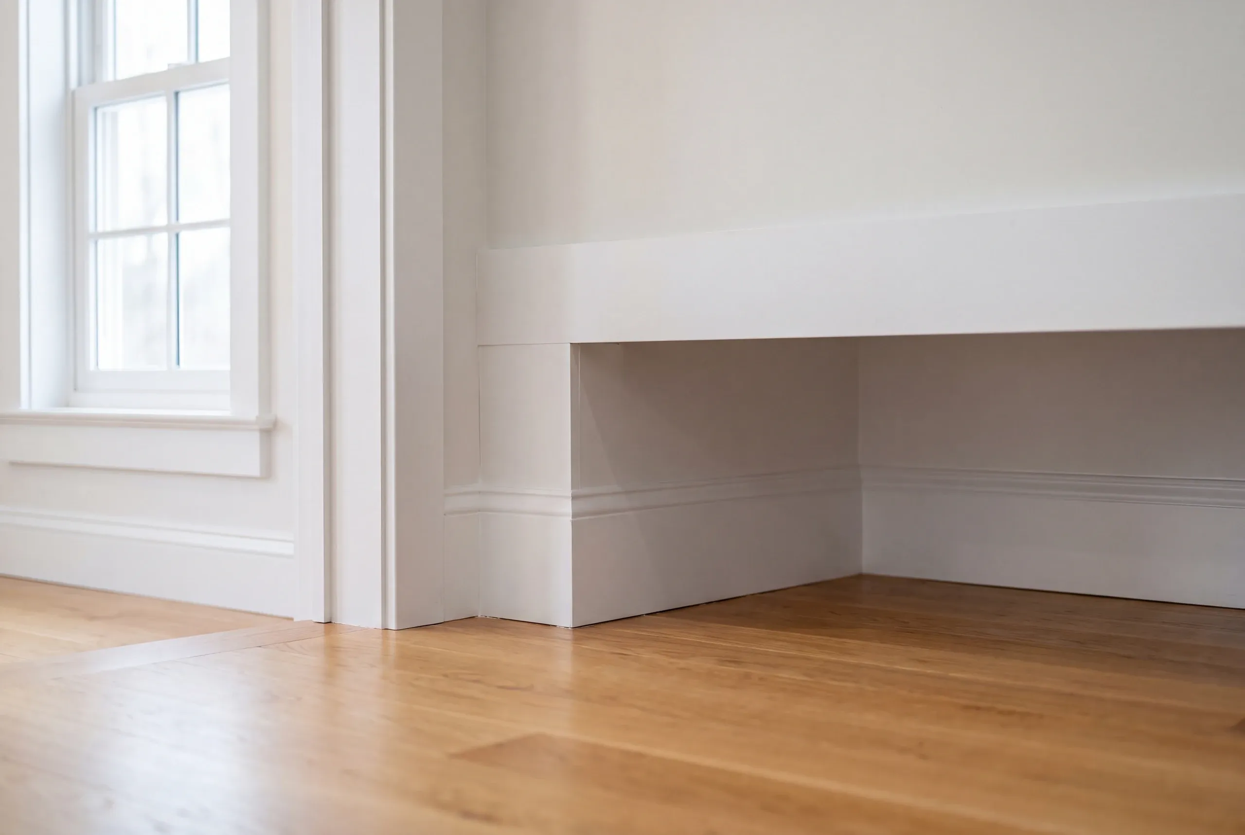 Home renovation contractor Searsmont Maine: built-in white bench with tall baseboard beside a double-hung window