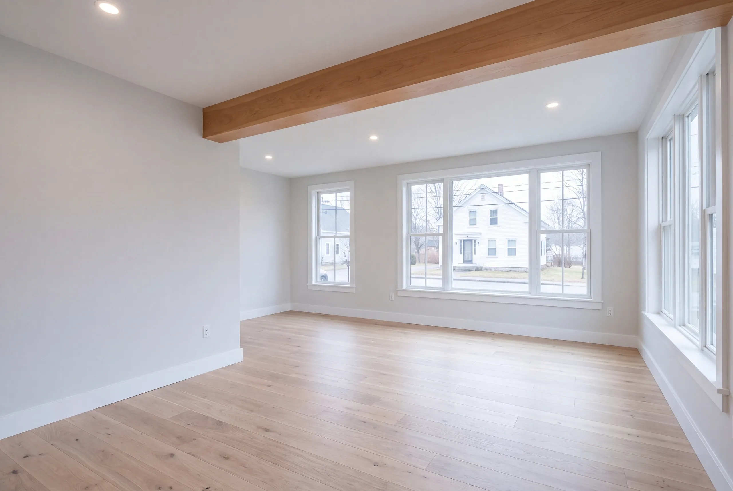 Remodeling company Thomaston Maine: bright empty room with an exposed wood beam, recessed lights and light oak floors