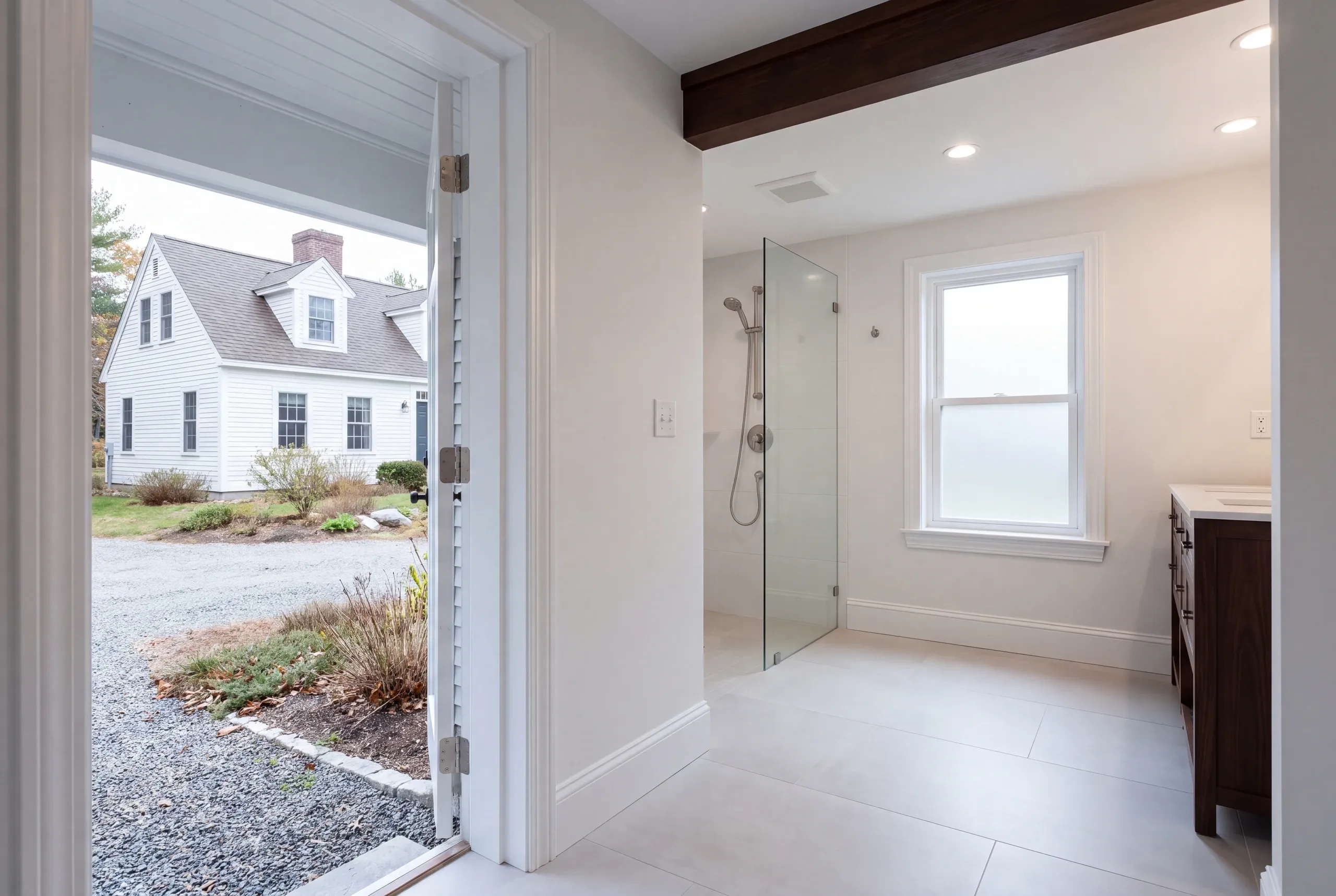 Remodeling company Warren Maine: curbless glass walk-in shower and wood vanity seen past an open door to a white cape
