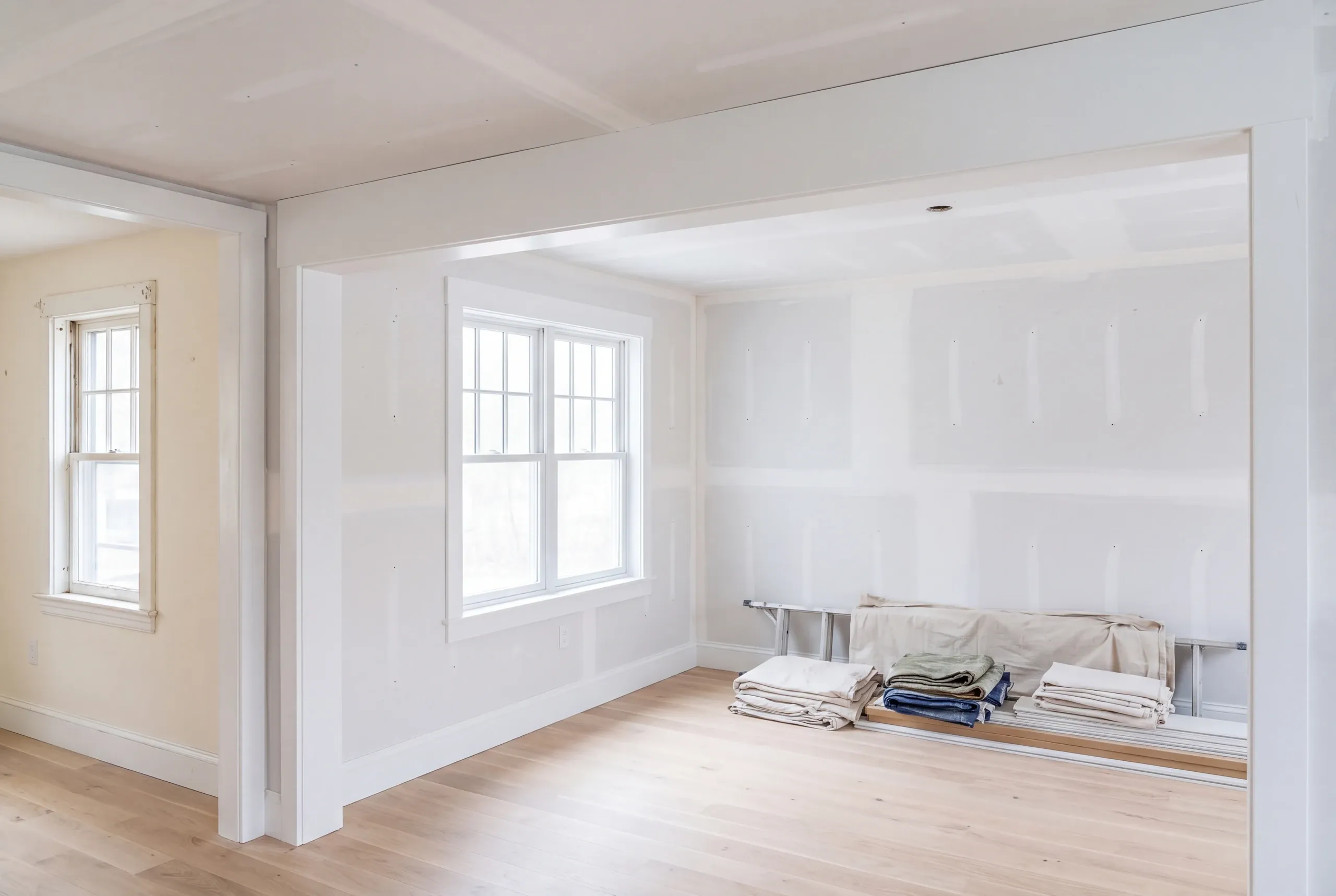 Home remodeling contractor Warren Maine: room mid-renovation with taped drywall seams, new trim and folded drop cloths on a bench