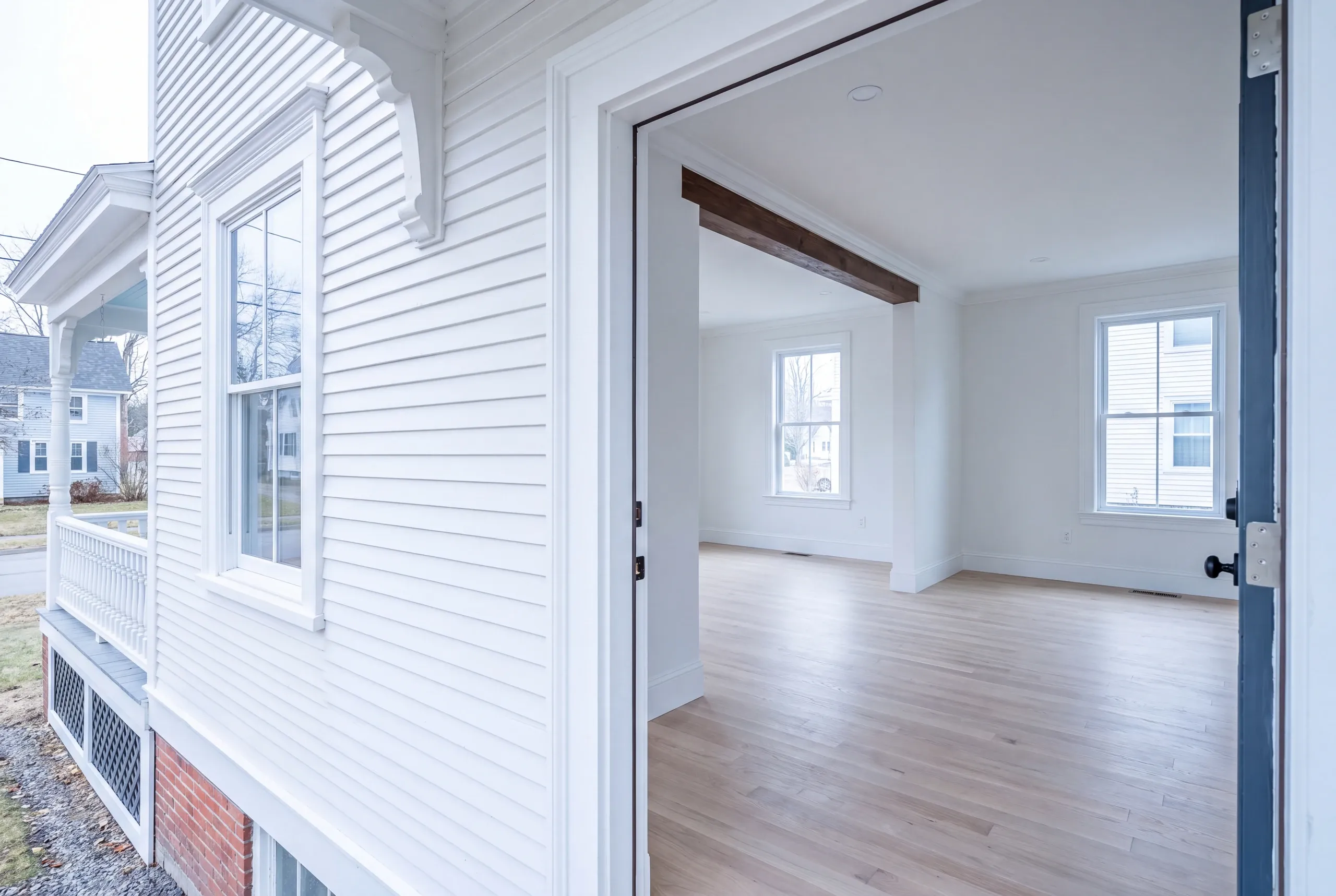Home remodeling in Waterville, ME: open door from a white clapboard Victorian porch side into an empty beamed room