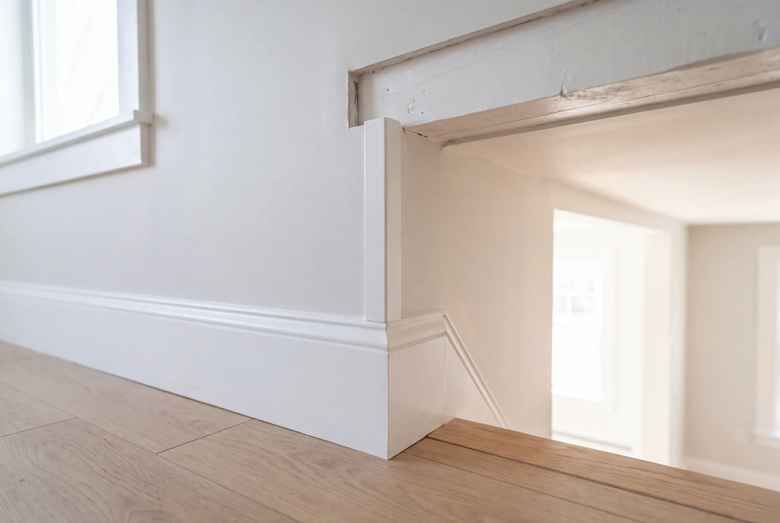 Home renovation contractor Waterville Maine: white baseboard and casing at a step-down opening under an old painted beam header