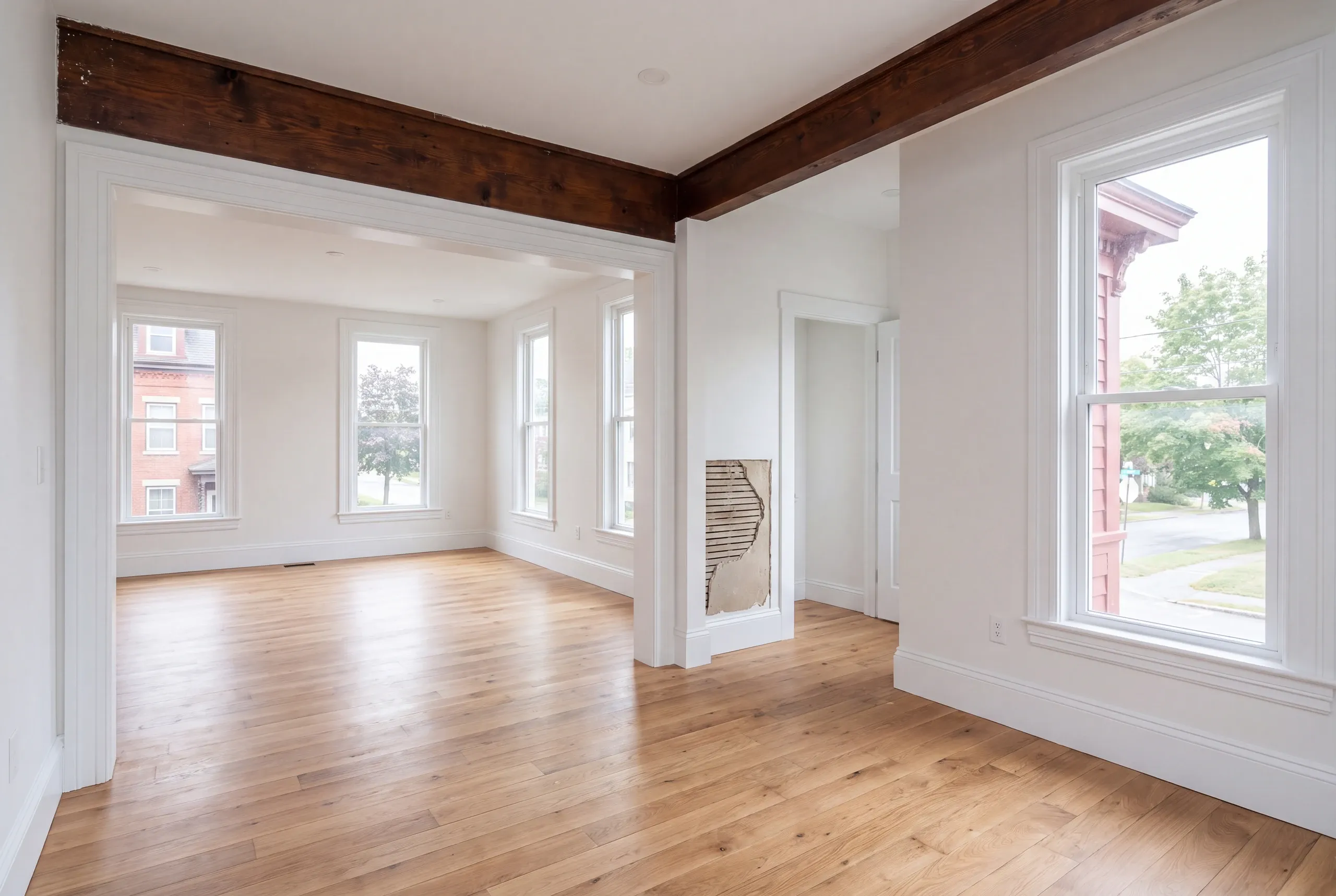 Remodeling company Waterville Maine: empty beamed room with oak floors and a patch of bare lath left open in one wall