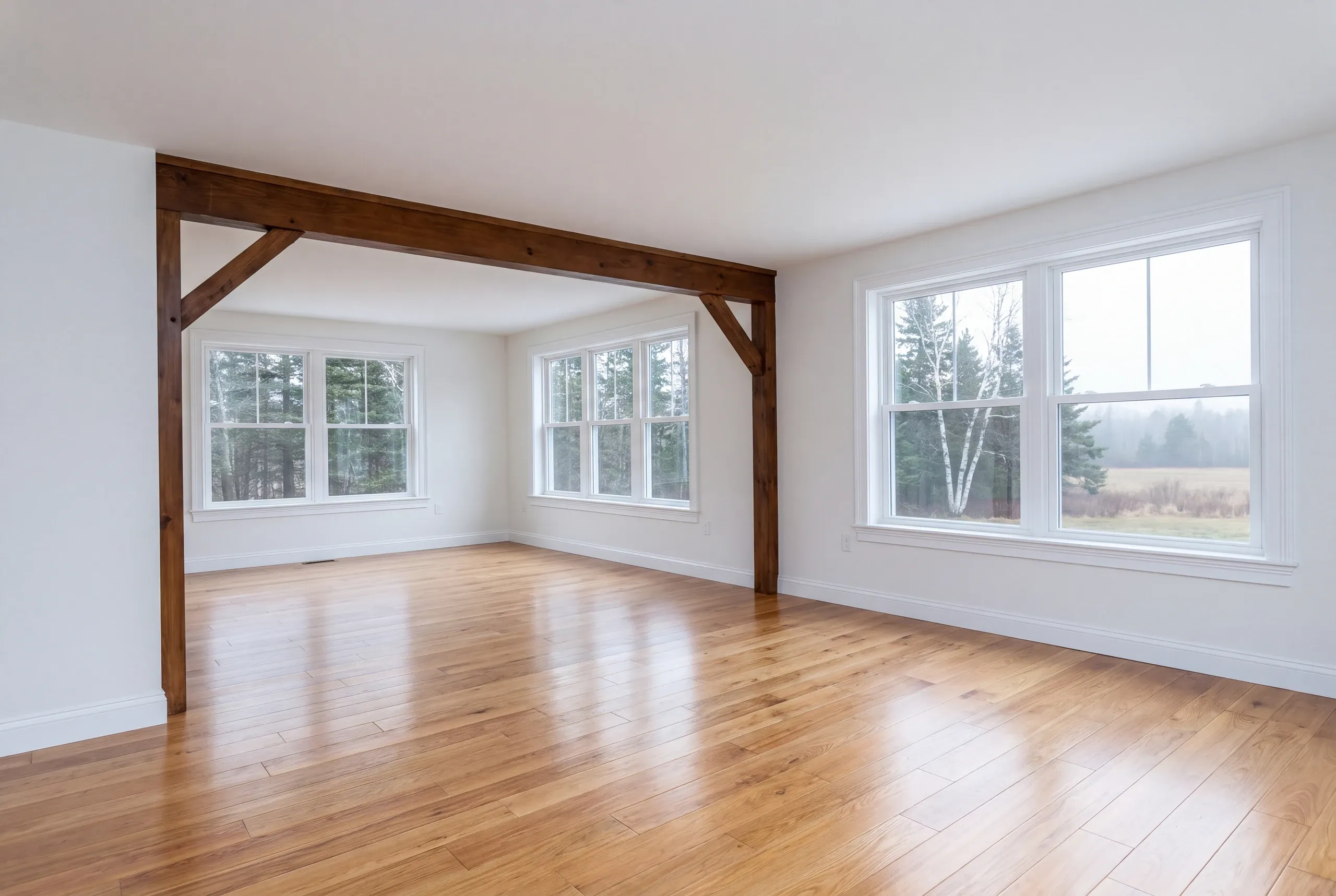 Home remodeling in Windsor, ME: empty room with a dark timber frame and knee braces, oak floor and field views