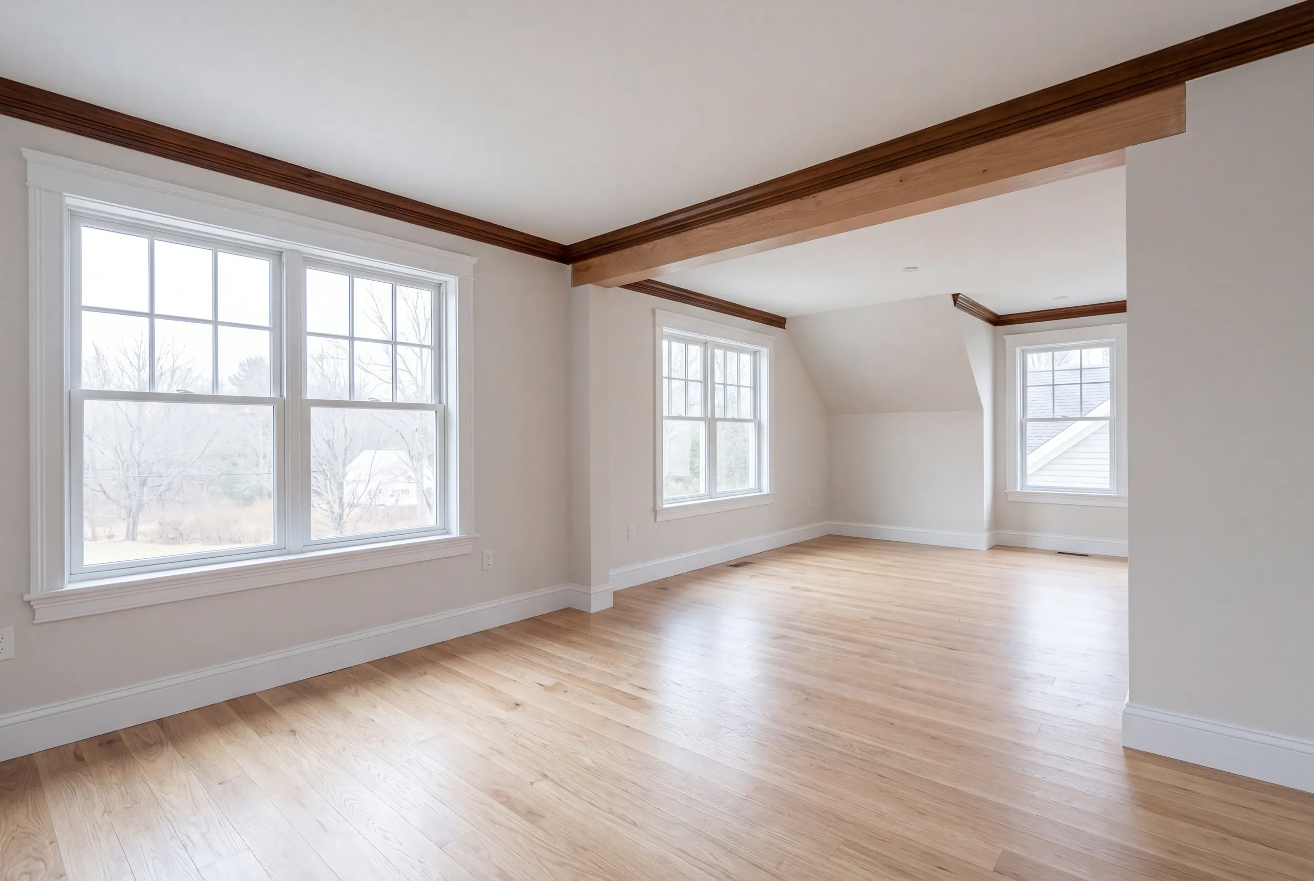Home renovation contractor Windsor Maine: empty room with dark wood crown and beam, oak floor and a sloped ceiling beyond