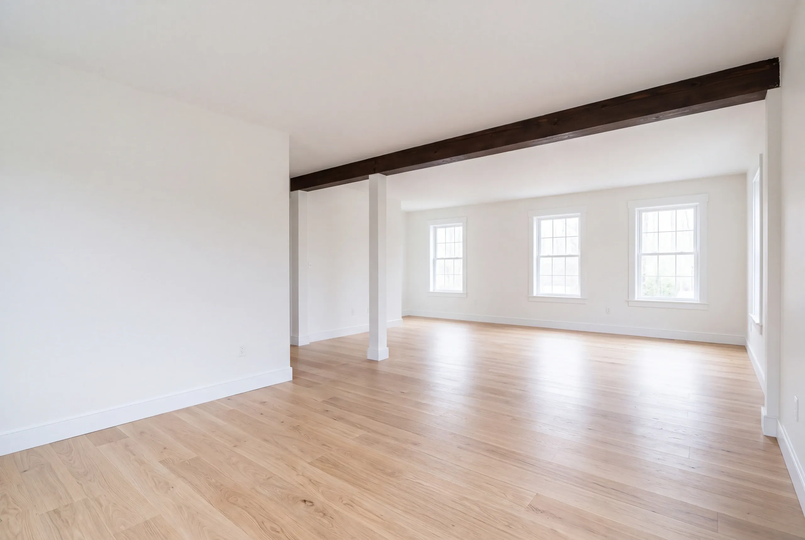 Remodeling company Windsor Maine: empty room with a dark beam on a white post, light oak floor and white walls