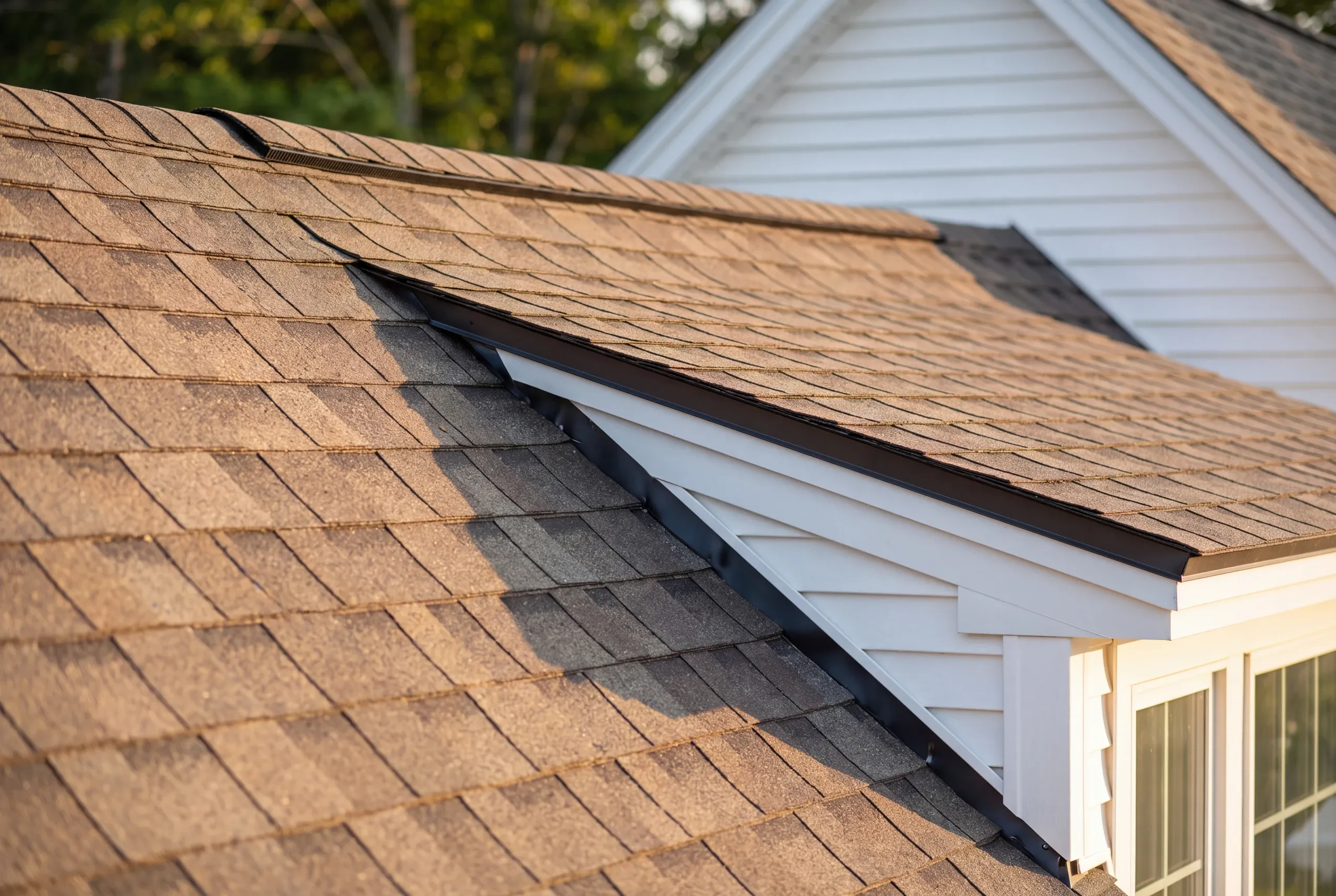 Residential roofing contractor Augusta Maine: close view of tan architectural shingles where a gable roof meets the main roof