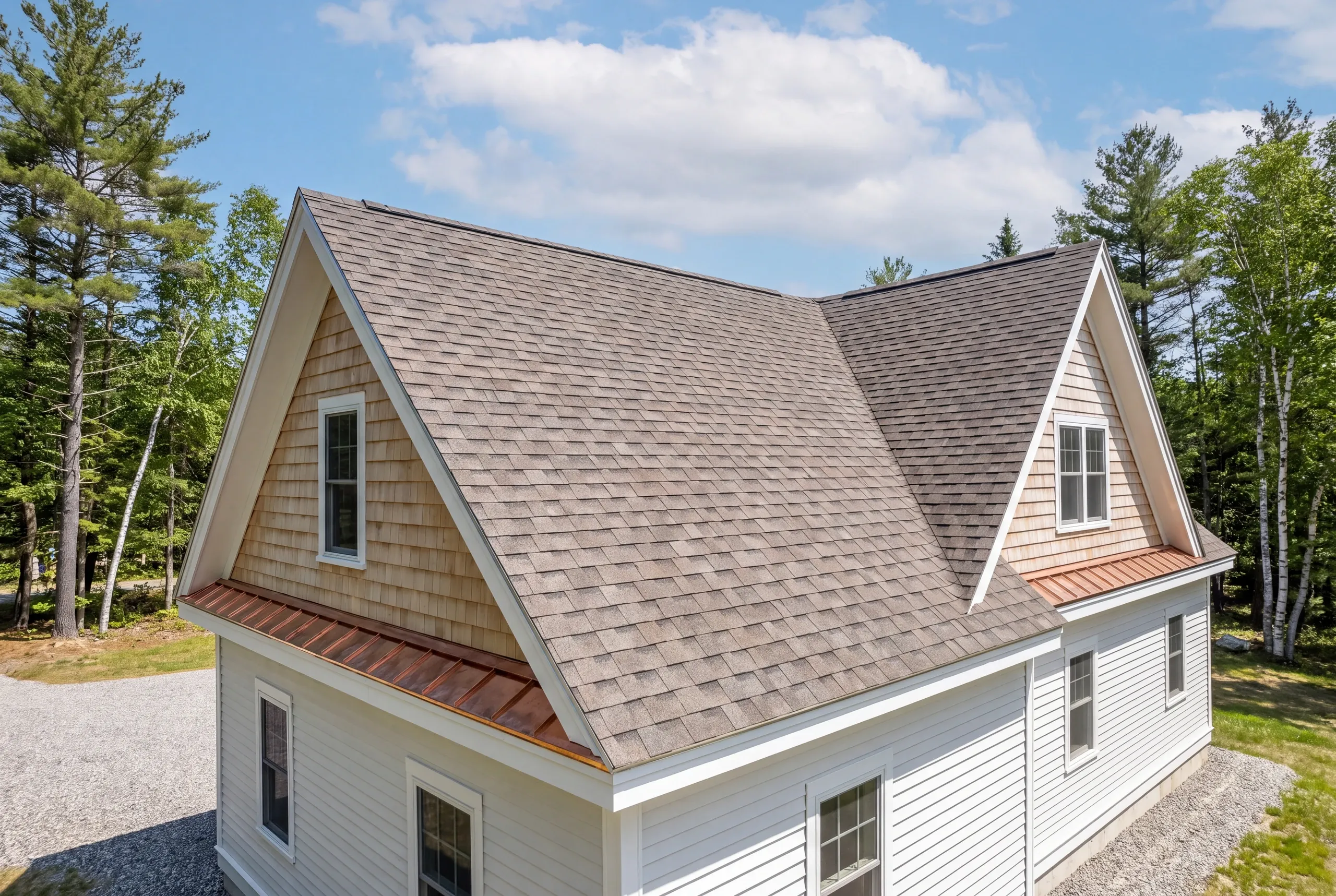 Residential roofing contractor Augusta Maine: white house with cedar-shingled gables, gray architectural shingles and copper eave trim