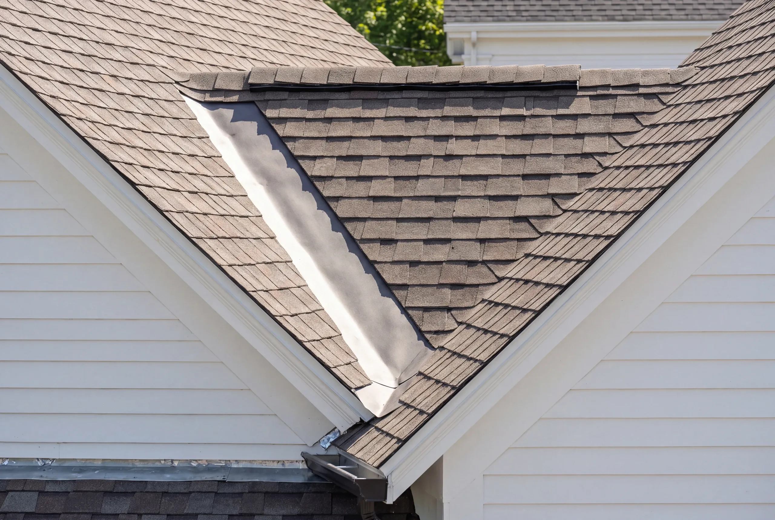 Residential roofing contractor Bath Maine: close view of an open metal valley between two shingled gables over white siding