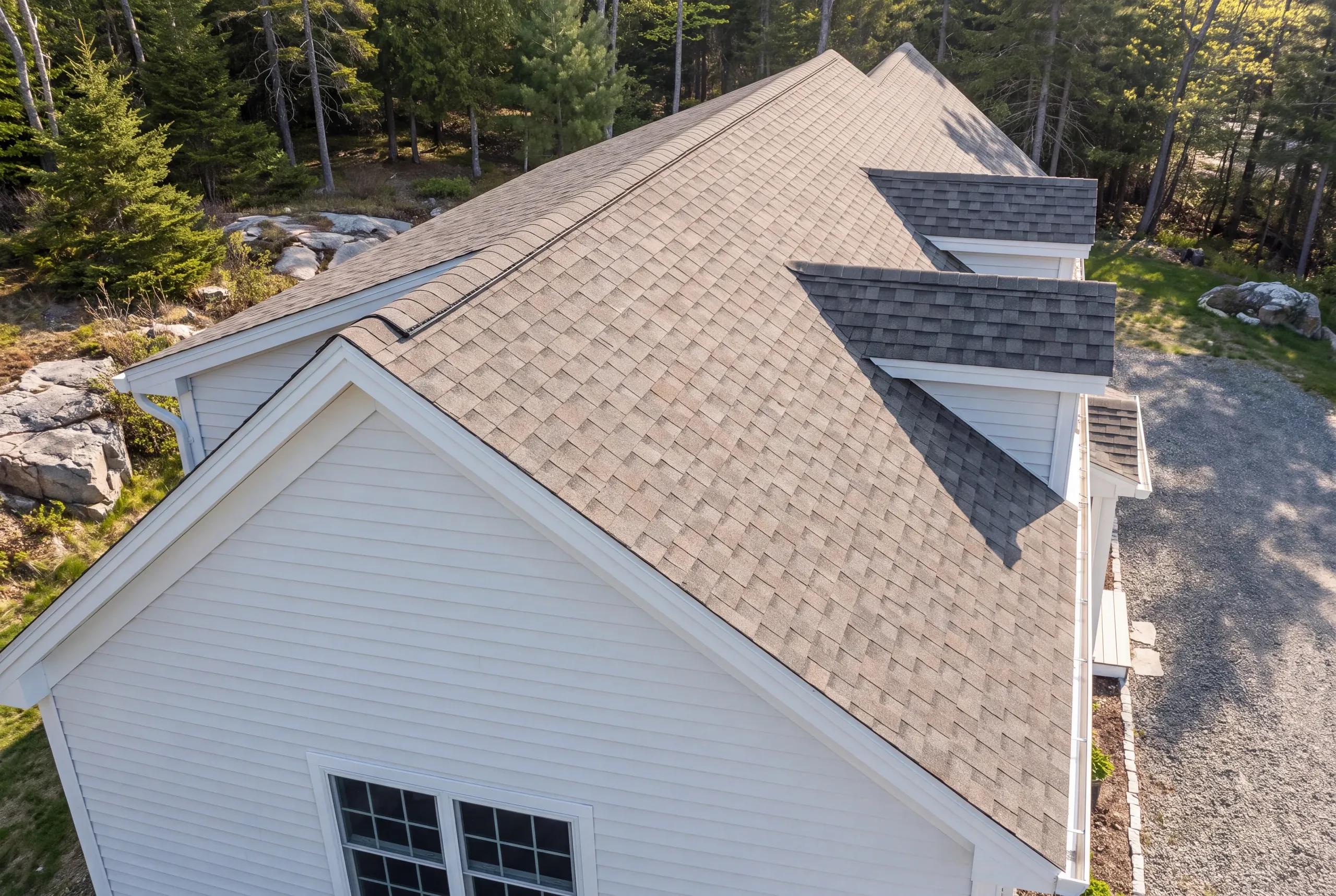 Residential roofing contractor Bucksport Maine: aerial view of a shingle roof with two gable dormers and ridge vent on a wooded lot