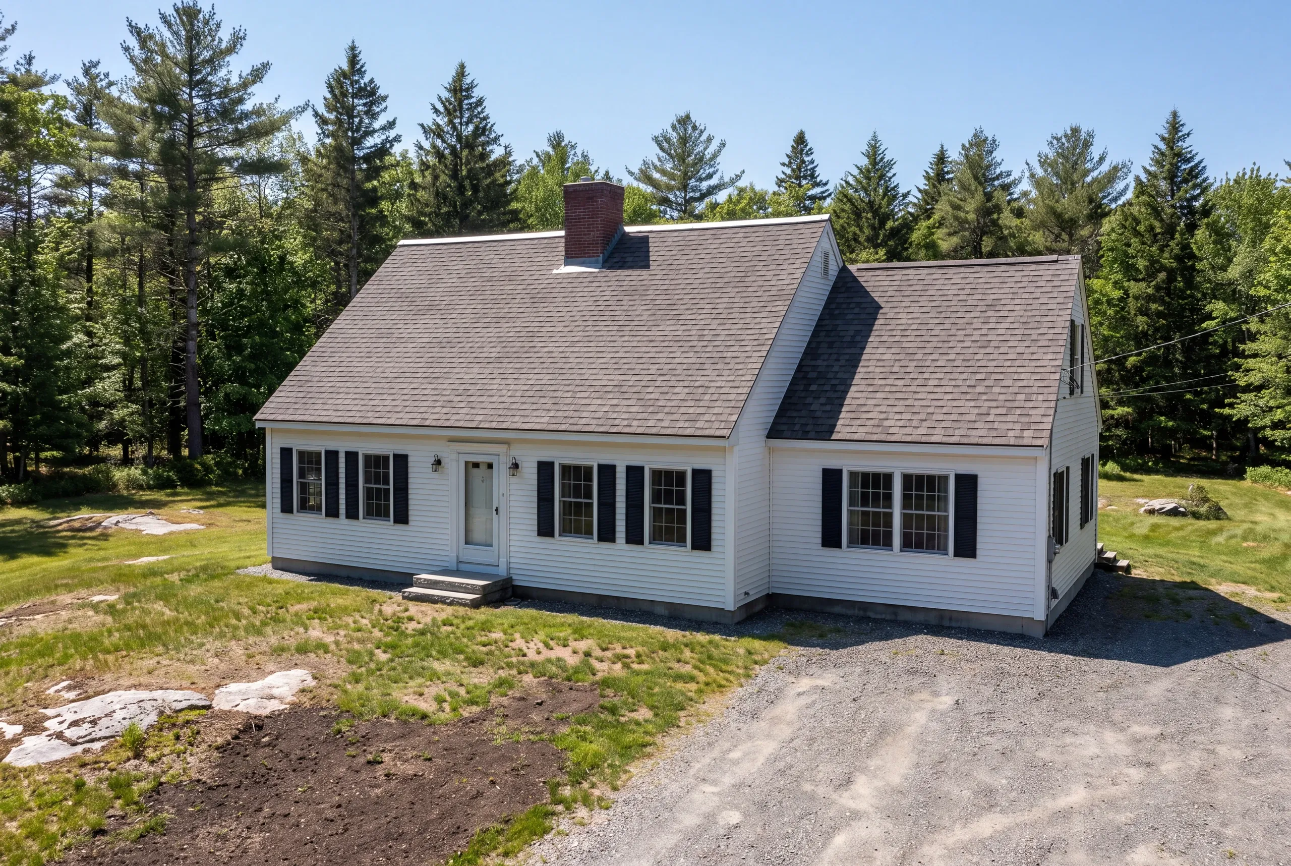 Roof replacement contractor Bucksport Maine: cape with a center brick chimney, black shutters and attached gable section on gravel