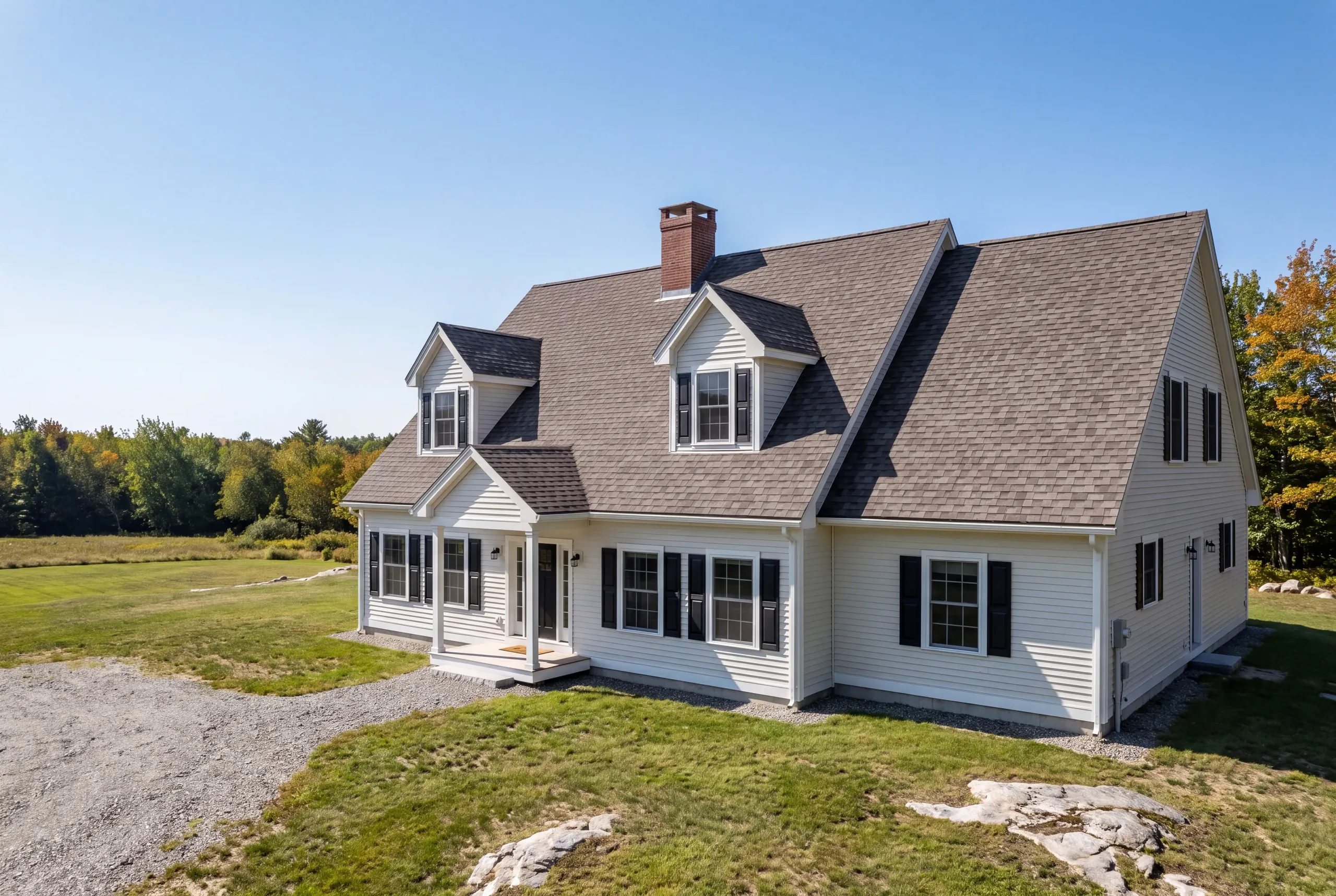 Roof replacement contractor Bucksport Maine: white cape with twin gable dormers and a full front porch facing an open field