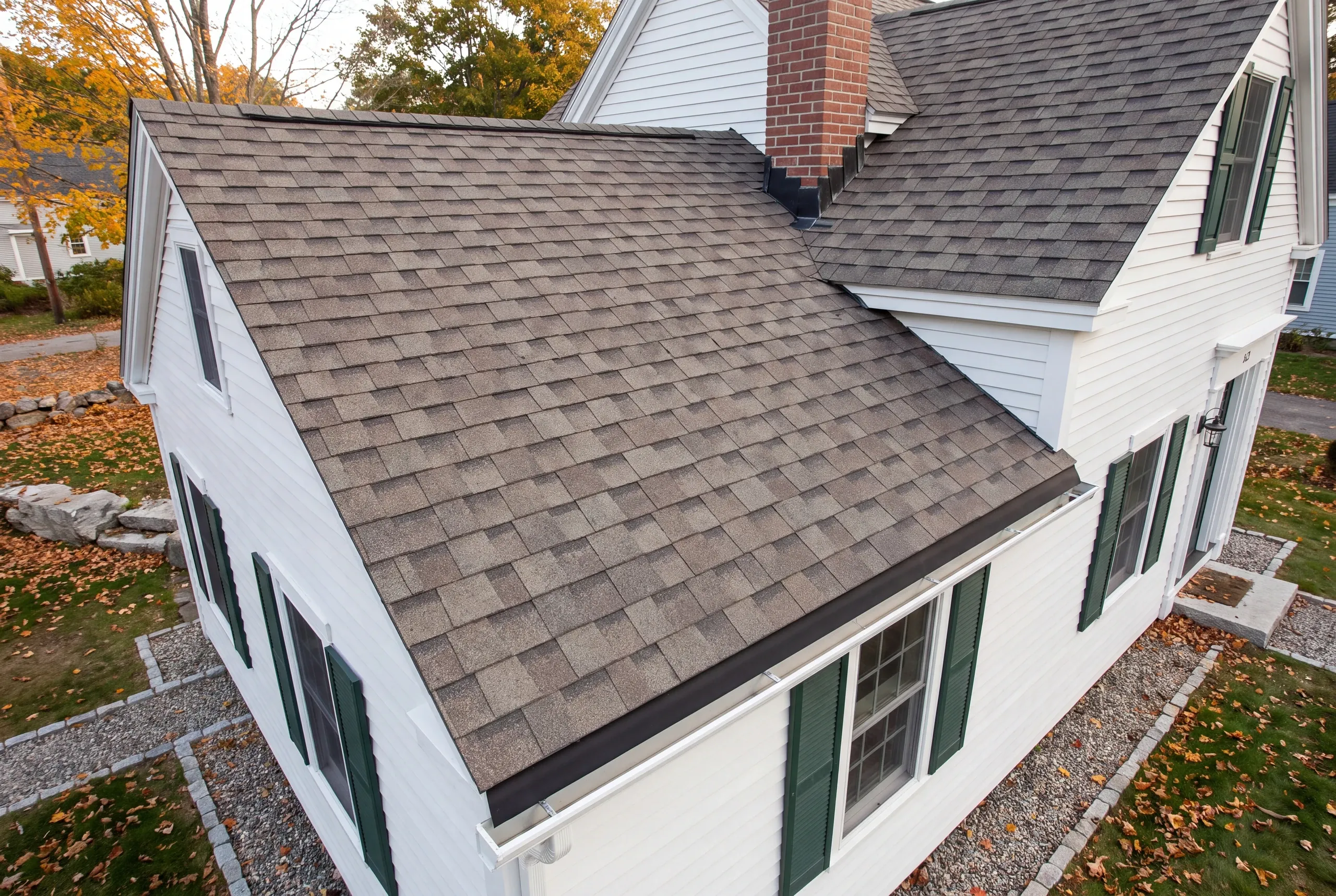 Residential roofing contractor Damariscotta Maine: aerial view of a white cape roof with brick chimney, step flashing and autumn leaves