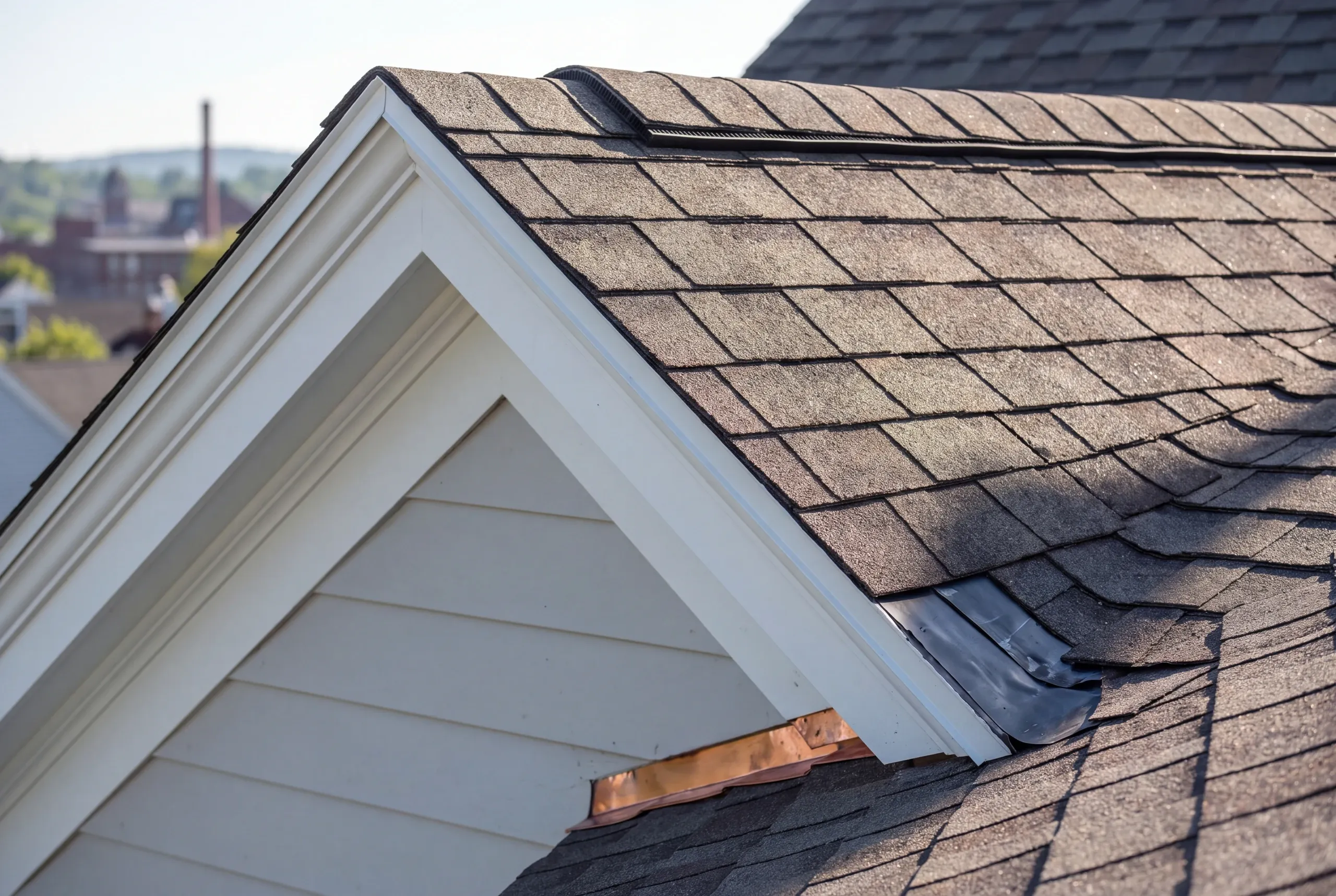 Residential roofing contractor Fairfield Maine: close view of a cross gable meeting the main roof with ridge vent and uneven shingles