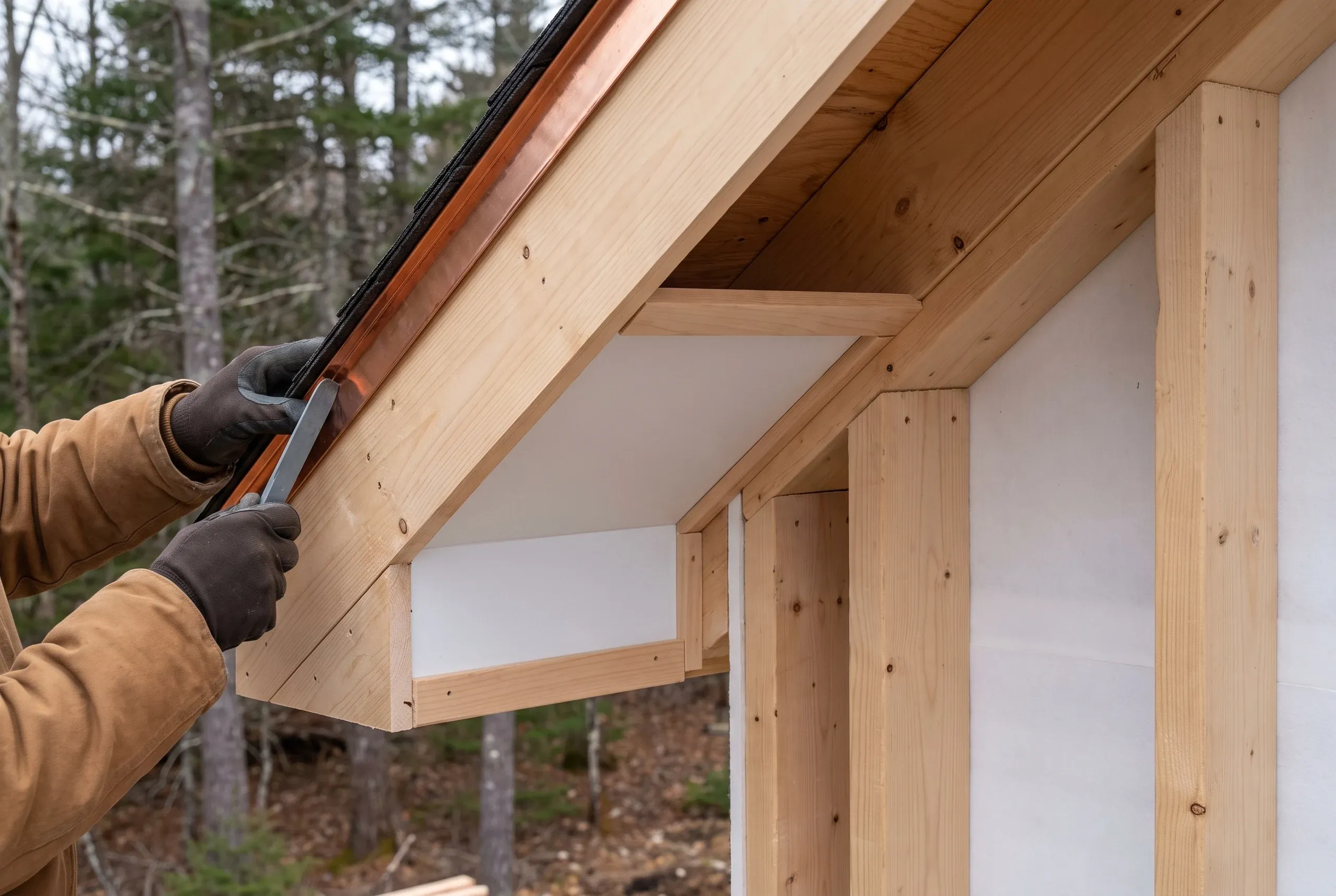 Residential roofing contractor Lincolnville Maine: gloved hands setting copper edge flashing along a rake above a boxed return
