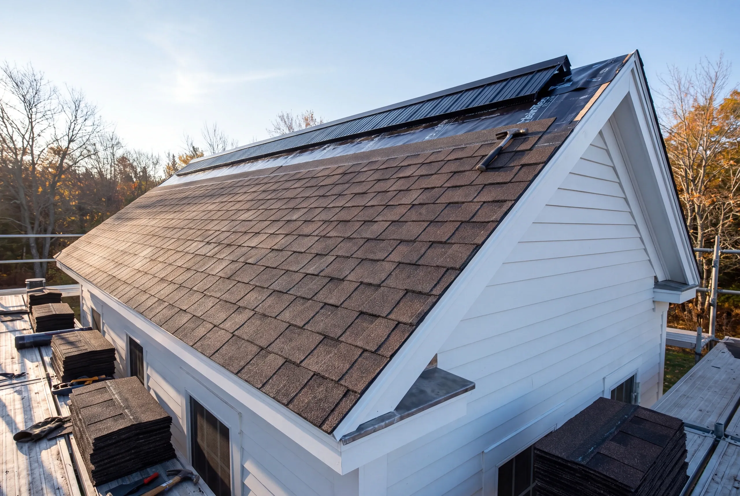 Roofing contractor Lincolnville Maine: partly shingled gable roof with bare underlayment near the ridge and bundles on staging