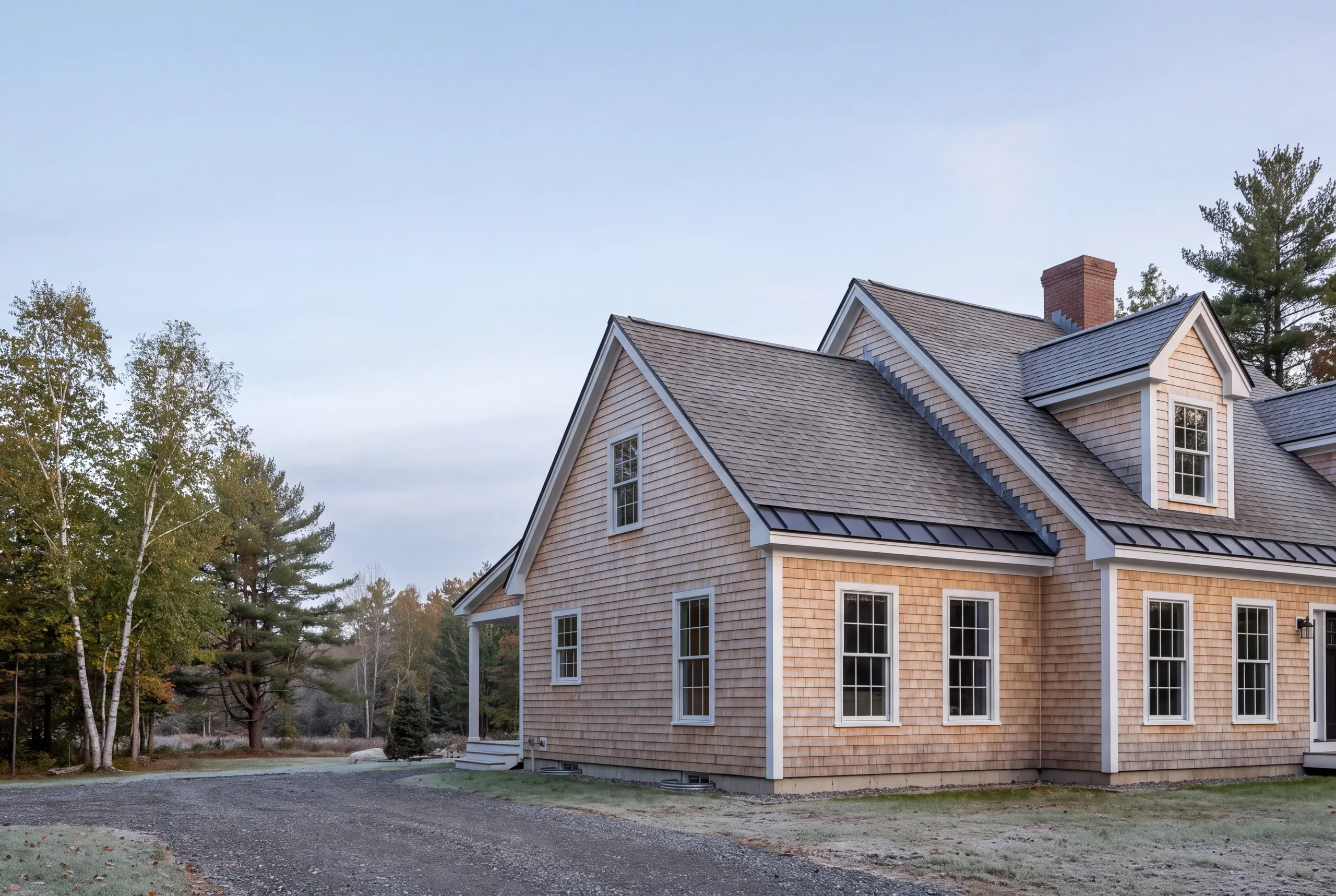 Roof replacement contractor Pittston Maine: cedar-shingle-sided cape with dormers, brick chimney and dark metal eave bands