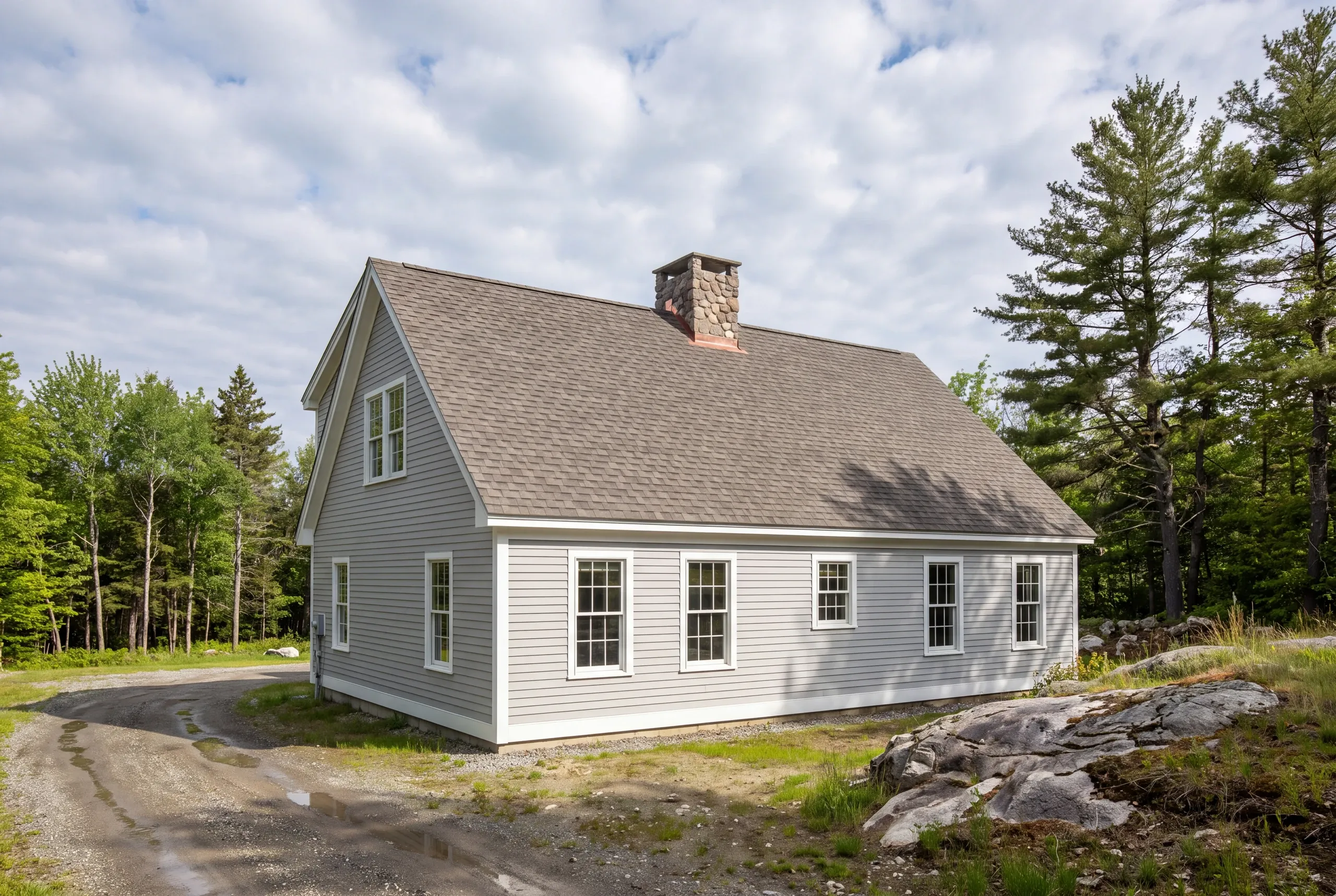 Roof replacement contractor Searsmont Maine: light gray lap-sided cape with brown-gray architectural shingles and a round fieldstone chimney
