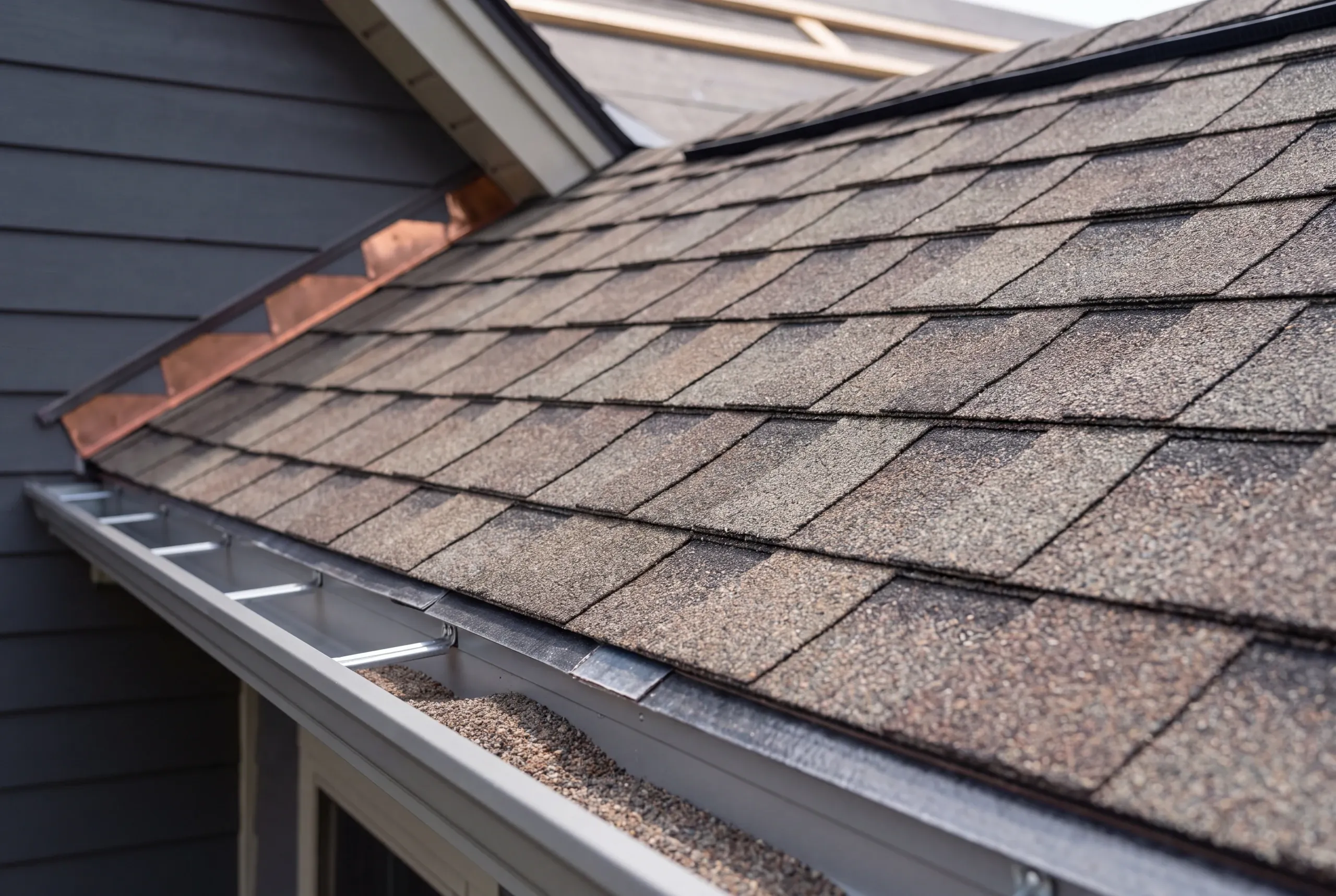 Residential roofing contractor Waldoboro Maine: eave of brown arch shingles with copper step flashing and loose shingle granules in the gutter