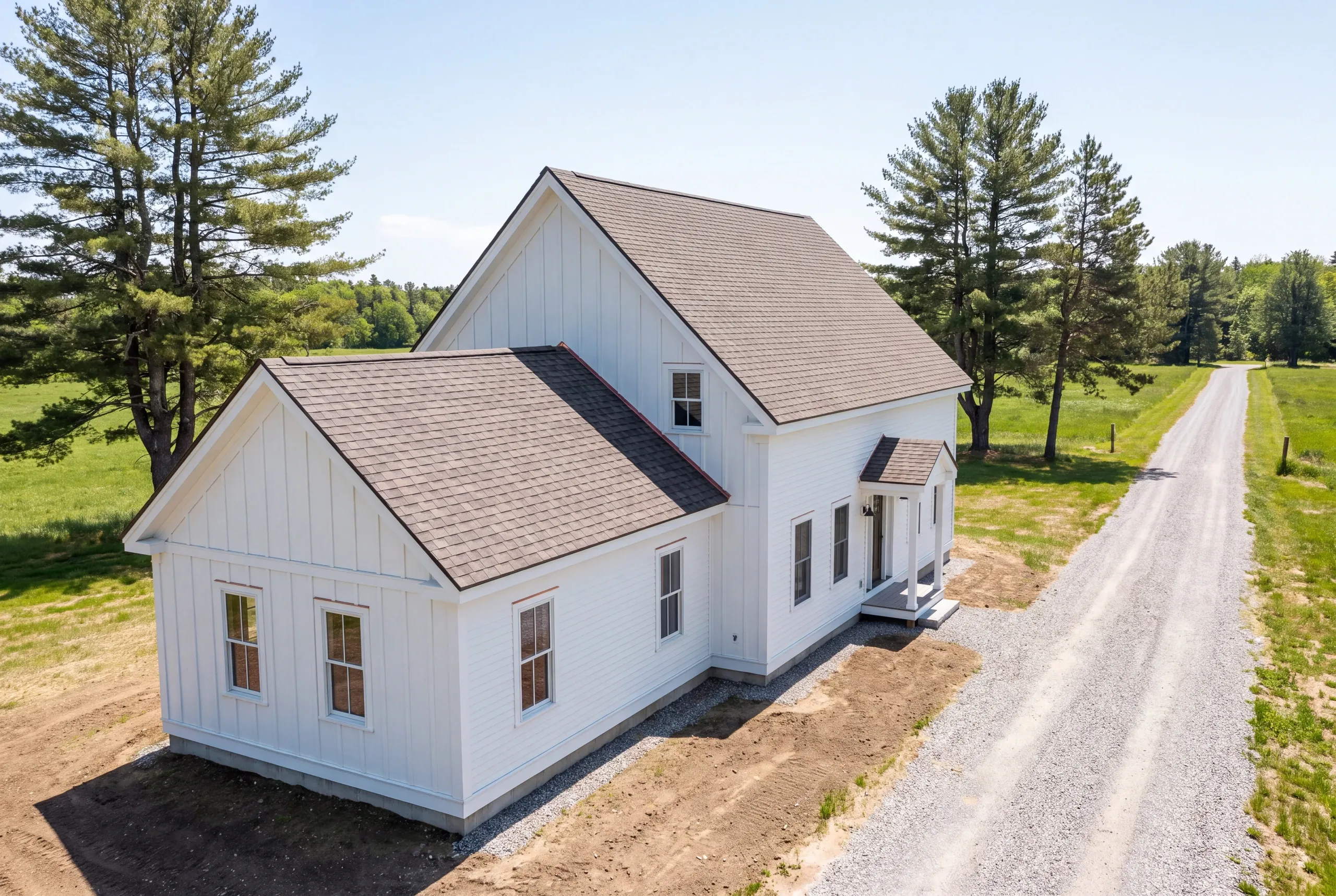 Roof replacement contractor Waldoboro Maine: white farmhouse with board and batten gables and brown arch shingles beside a long gravel drive