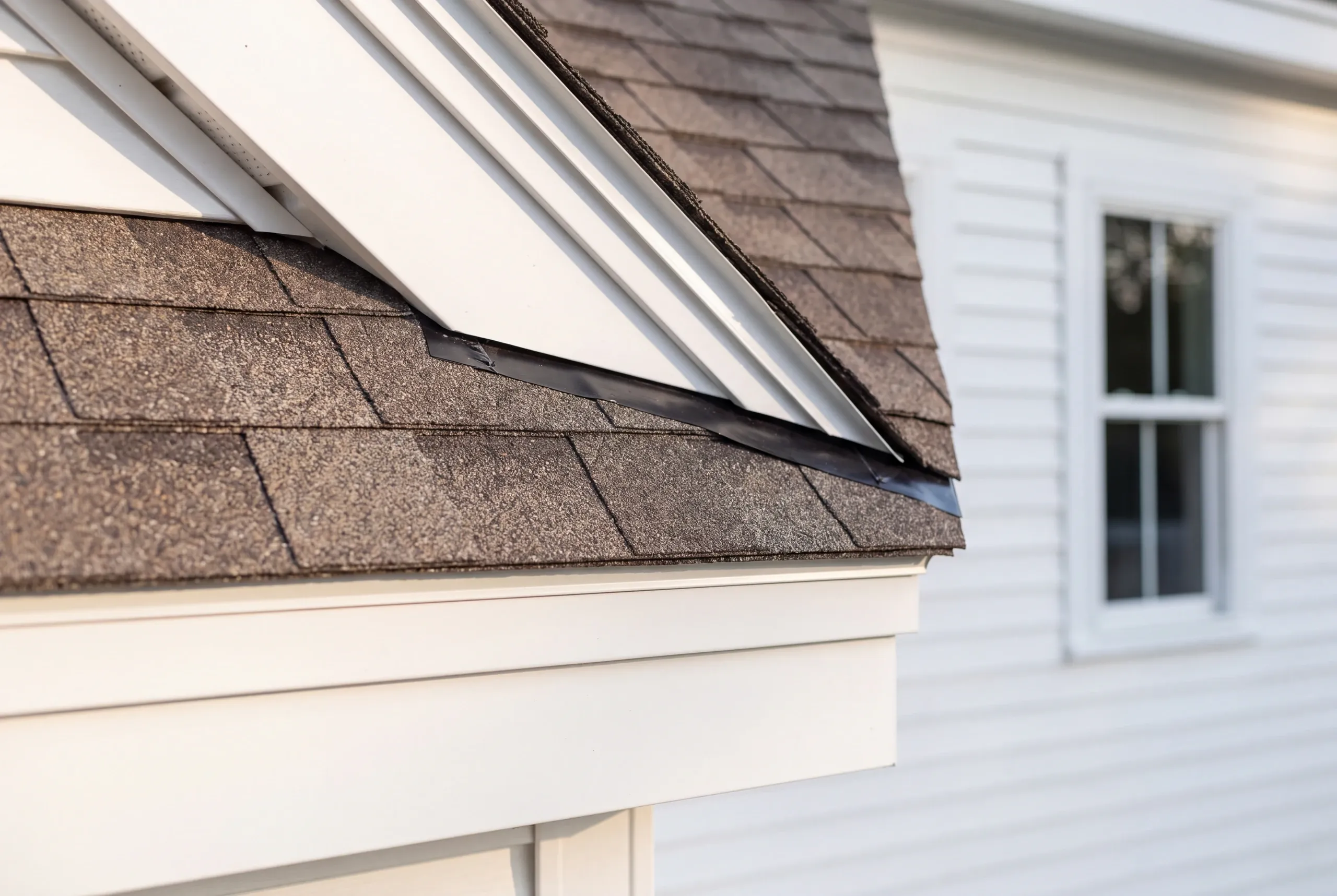 Residential roofing contractor Warren Maine: gable rake meeting a lower shingle roof with a black flashing strip and white rake trim