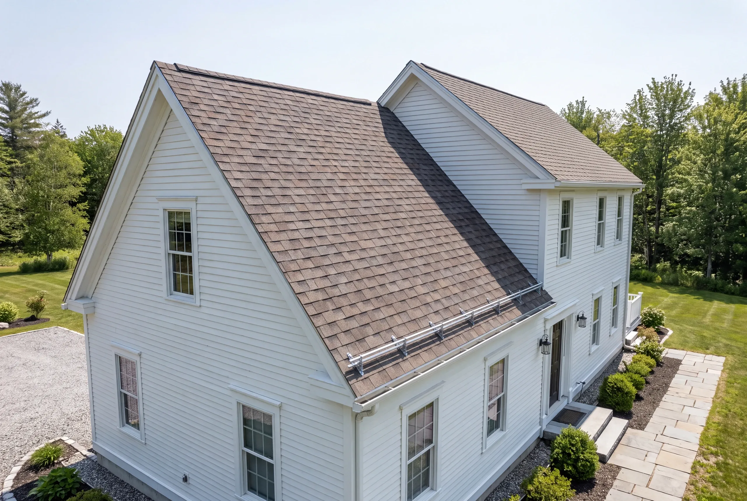 Roof replacement contractor Windsor Maine: white two-story house with gray-brown arch shingles and a snow guard rail above the front entry