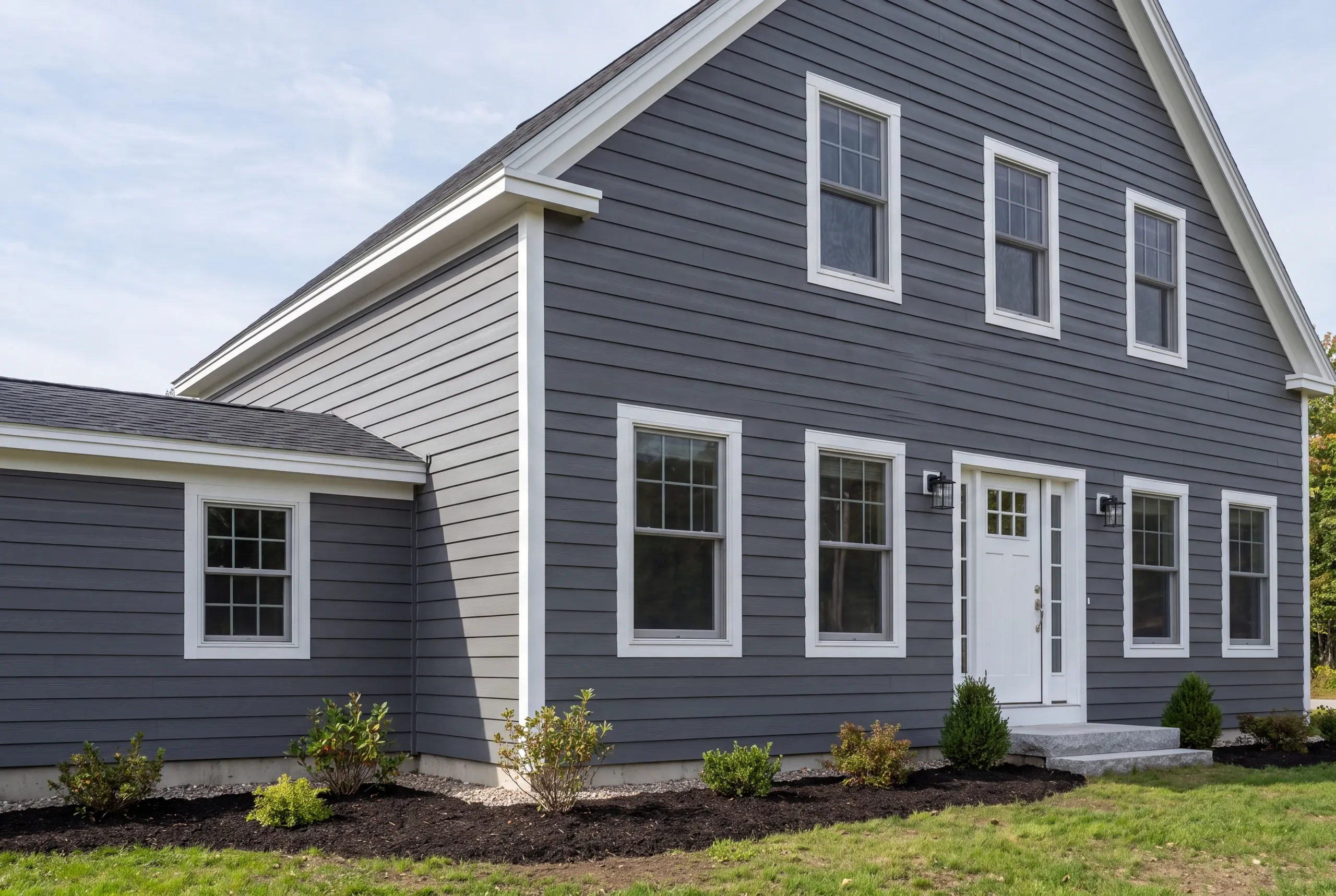 Exterior siding contractor Augusta Maine: dark gray lap-sided gable-front house with a lighter connector, white door and new shrubs