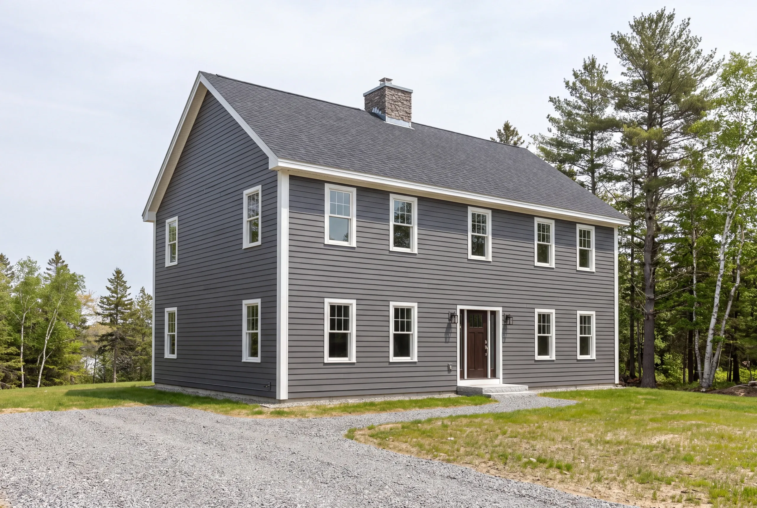 Siding contractor: two-story colonial in dark gray lap siding with a stone chimney and gravel drive among pines