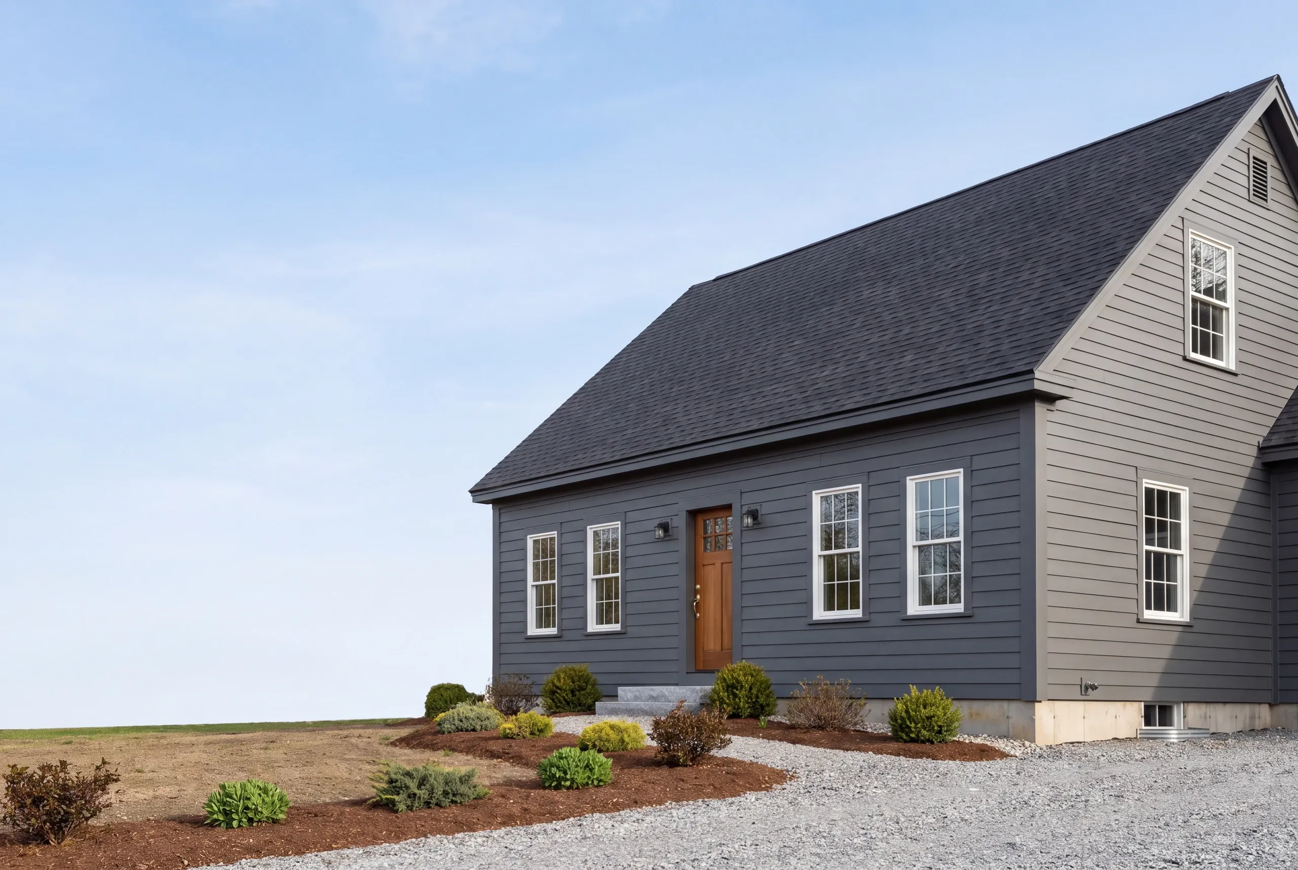 Exterior siding contractor Pittsfield Maine: cape with charcoal lap siding front, lighter gray gable end and new plantings by a field