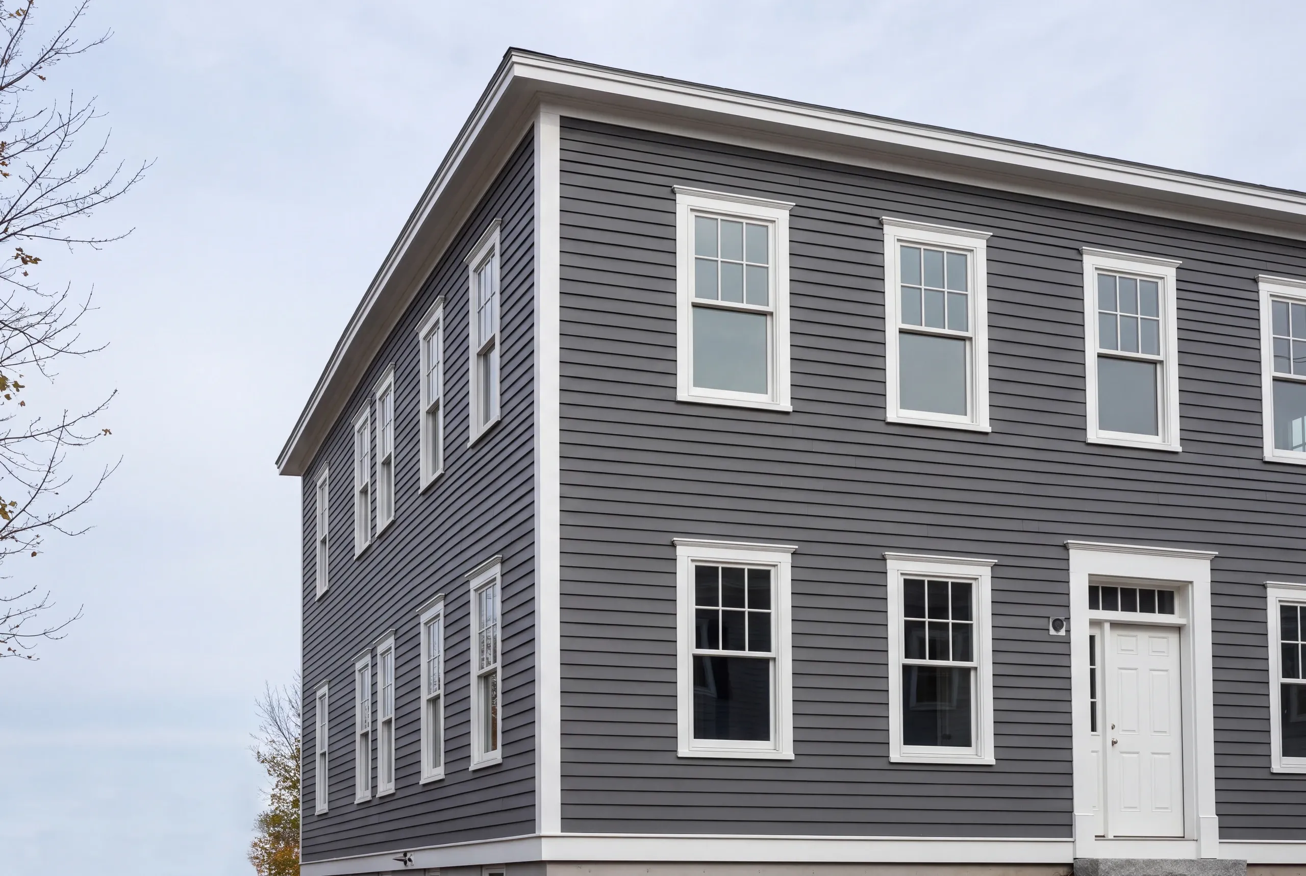 Exterior siding contractor Waterville Maine: low view of a boxy two-story house in gray lap siding with white windows and a transom door
